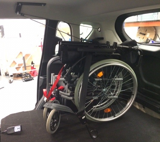 A folded wheelchair in the back of an adapted van, attached securely to a ceiling hoist.