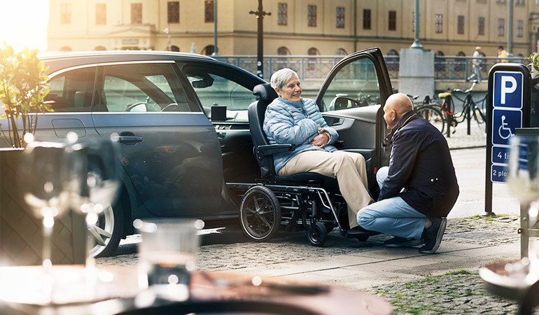 In a city centre, a wheelchair user is loading into a car using a Carony transfer system.