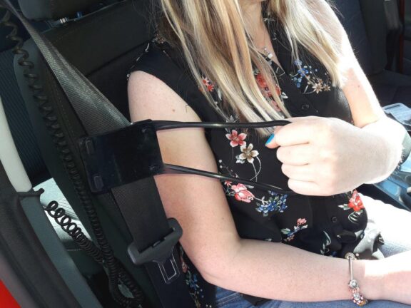 A driver using a seat belt grabber handle to more easily reach a seatbelt by reaching across themself.