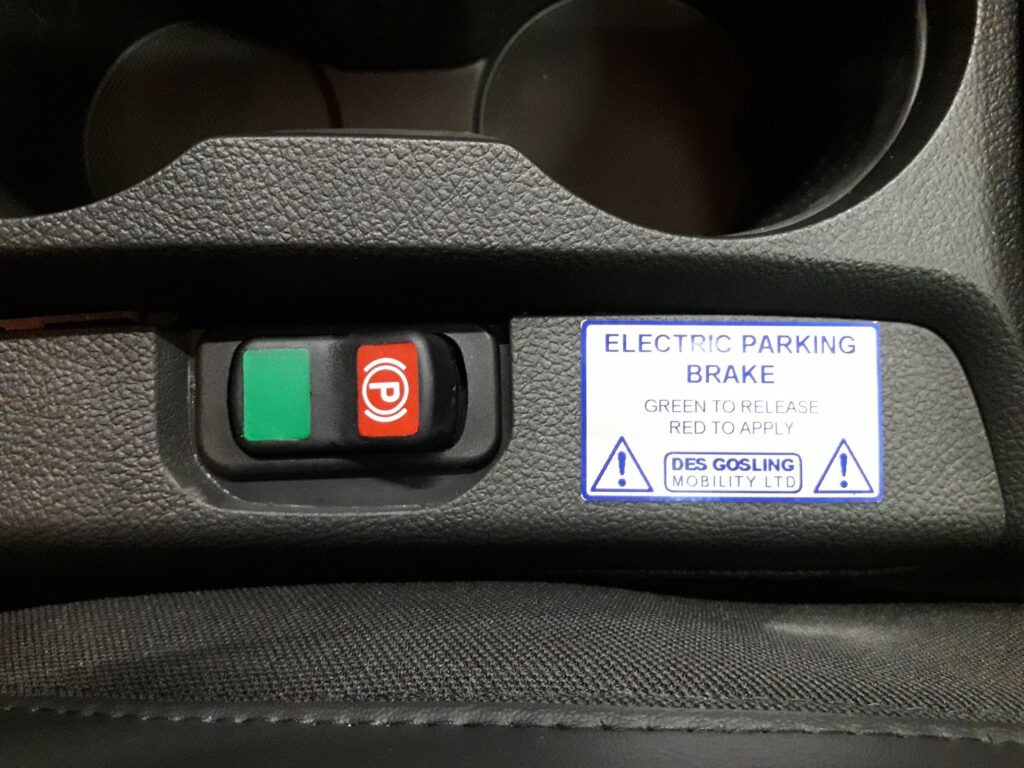 Closeup of Electric Handbrake switch with a warning label.
