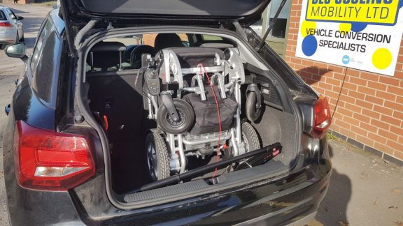 A folded mobility scooter in an open car boot with a stowed Brig Ayd 40kg hoist.
