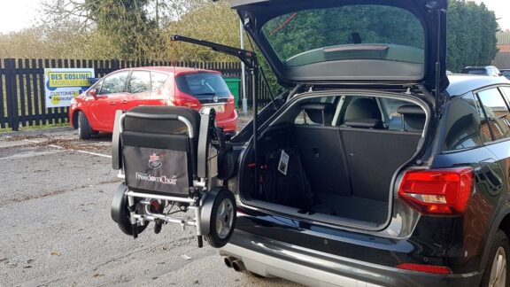 Brig Ayd 40kg Folding Hoist lifting a folded electric wheelchair into a car boot.