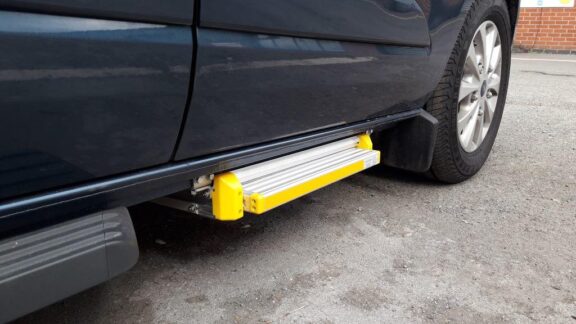 Electronic Side Step shown under a closed driver's side door, in the stowed position so it does not extend out past the footprint of the car.