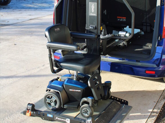 A joey lift is lowered out of the back of a blue van, with a scooter loaded.