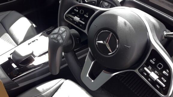 Closeup of Mercedes steering wheel fitted with a Smartsteer controller. It is shaped to be gripped with one hand while operating various car controls at the top with the thumb.
