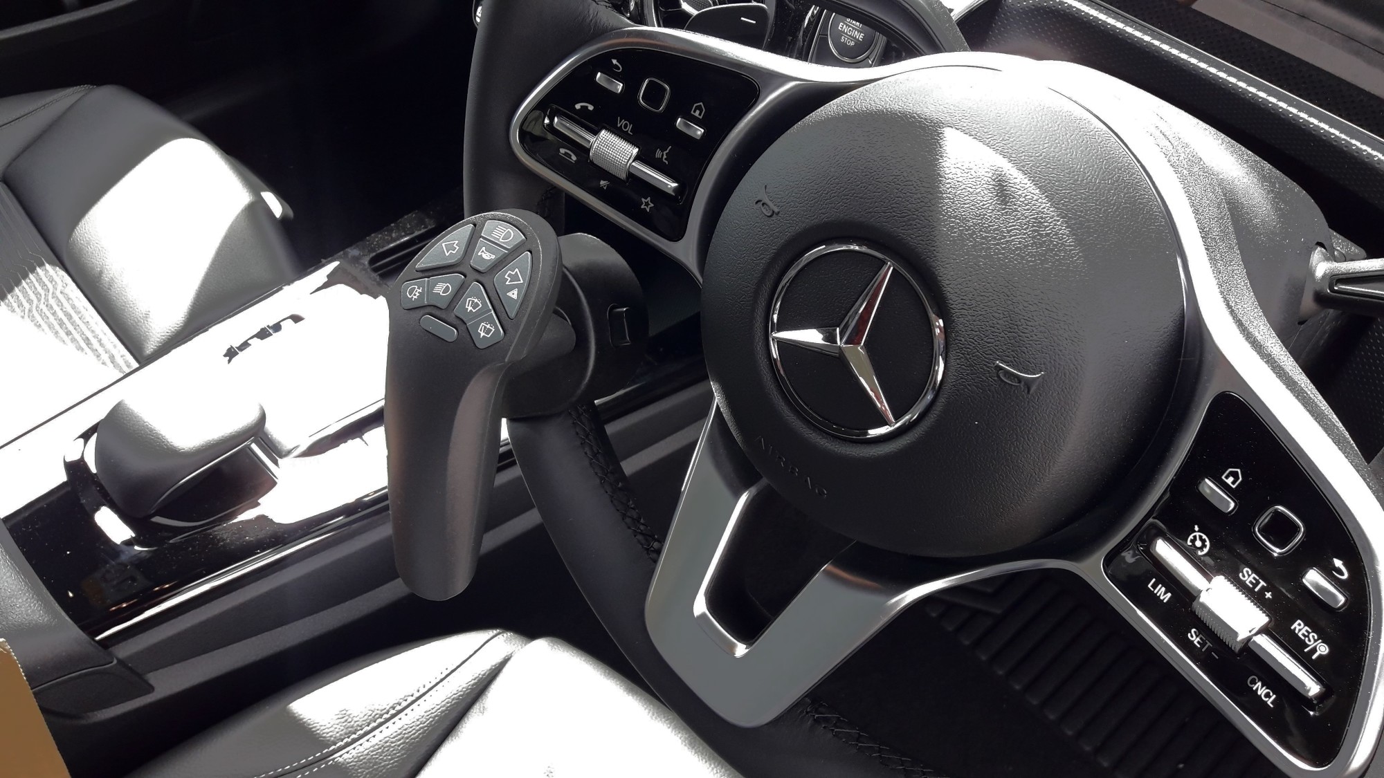 Closeup of Mercedes steering wheel fitted with a Smartsteer controller. It is shaped to be gripped with one hand while operating various car controls at the top with the thumb.