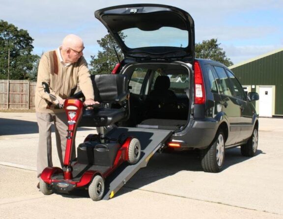 A mobility scooter is reversed up a portable ramp into an open car boot.