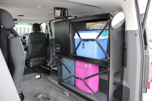 WAV Store shown in the back of a van. The unit is a black shelf with straps to keep various suitcases and containers in place during transit.