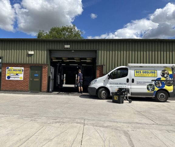 Des Gosling Mobility Workshop front, with a work van parked outside. A roller door is open with another van being worked on inside.