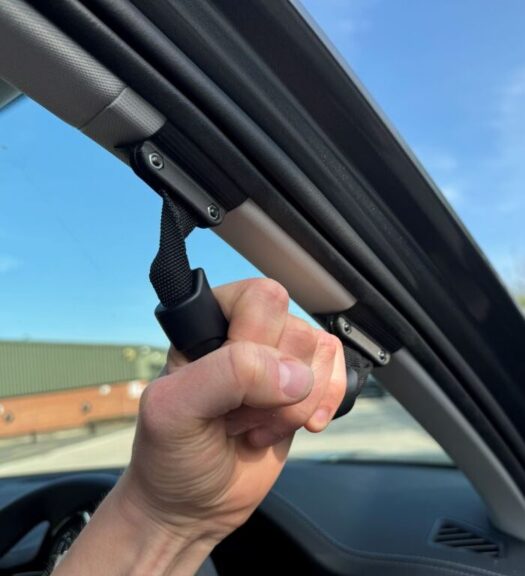 Close up of a hand grasping the grab handle attached to the A-pillar of a car on the driver's side.