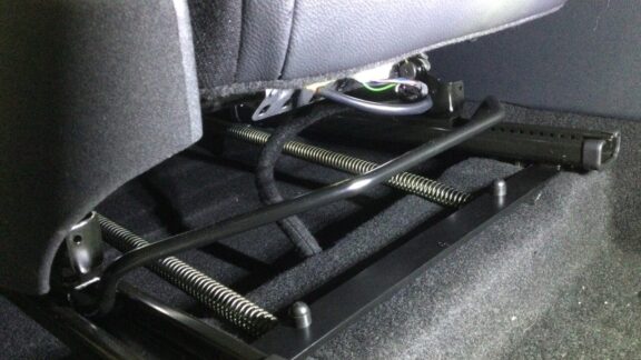 The spring mechanism of the assisted seat slide is shown underneath a front car seat.
