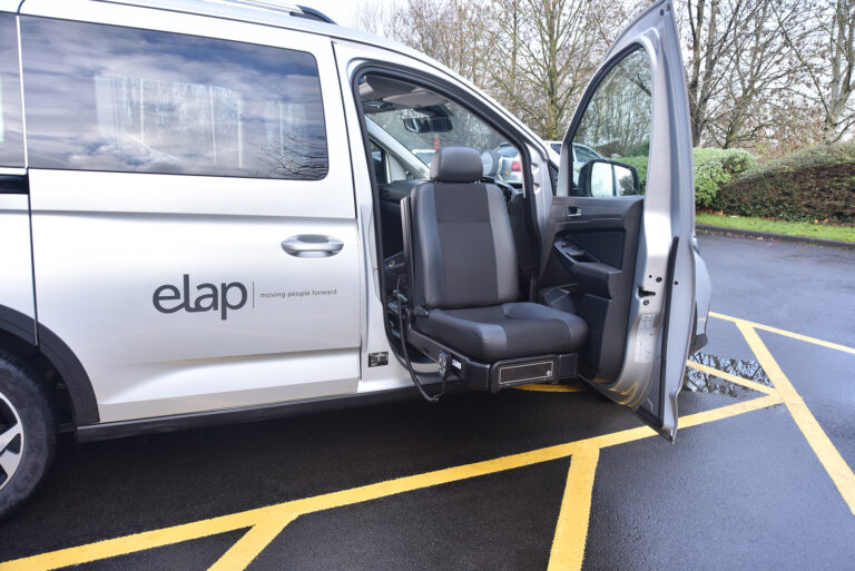 E-motion X swivel seat is shown extended through the driver's side door. A wired handset remote is attached to the edge of the seat.