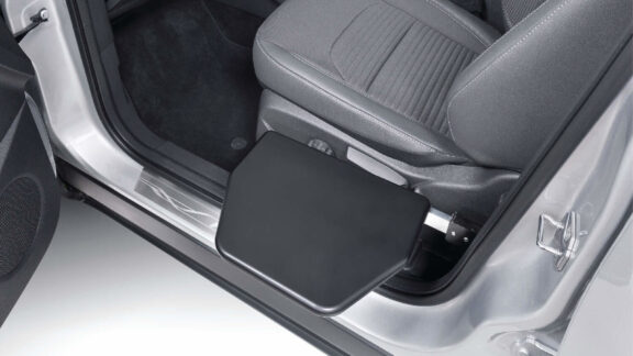 The manual transfer plate is shown slotted into place next to the passenger seat, leaving a smooth black surface level at seat height.