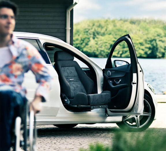 An open car door has a Turny low swivel seat rotated out through it. A wheelchair user is in the foreground.