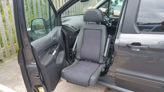 The Turney low vehicle swivel seat is extended out of the front passenger side door with armrests in the upright position.