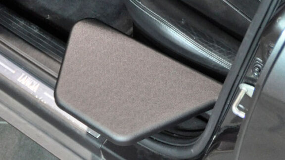 The Kivi tip up plate is shown next to a car seat. A small, black, smooth, trapezoid level with the edge of the seat.