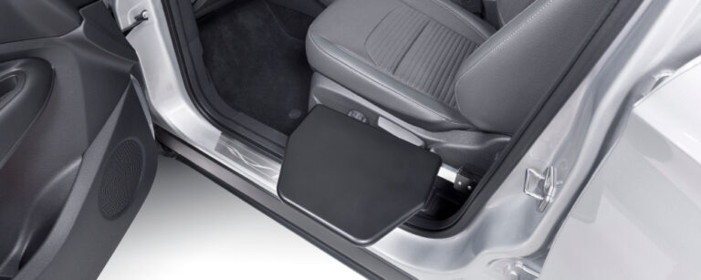 The manual transfer plate is shown slotted into place next to the passenger seat, leaving a smooth black surface level at seat height.
