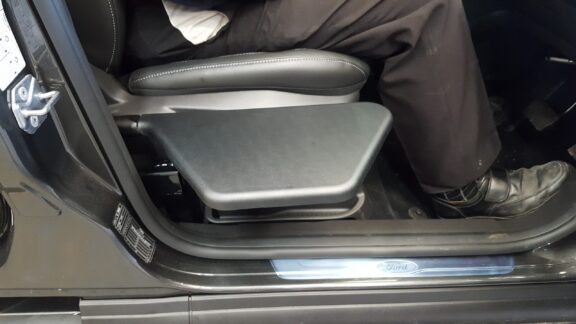 The Kivi Tip up plate is shown when unfolded protruding into the open car doorway, with a driver sat in the seat.