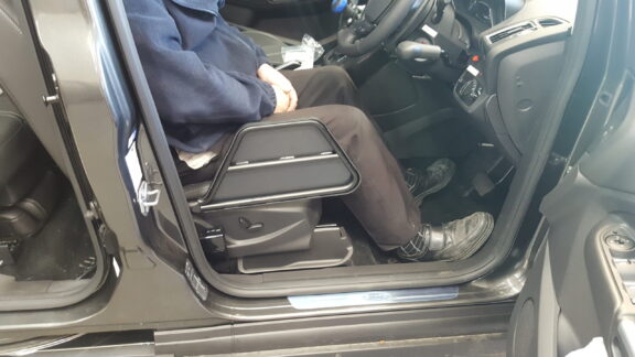 The Kivi Tip up plate is shown when folded up out of the way of the car door, with a driver sat in the seat.