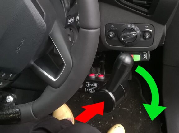 The radial accelerator is shown installed by a steering wheel with a red arrow showing the direction of the braking action and a green arrow showing the direction of the acceleration action.