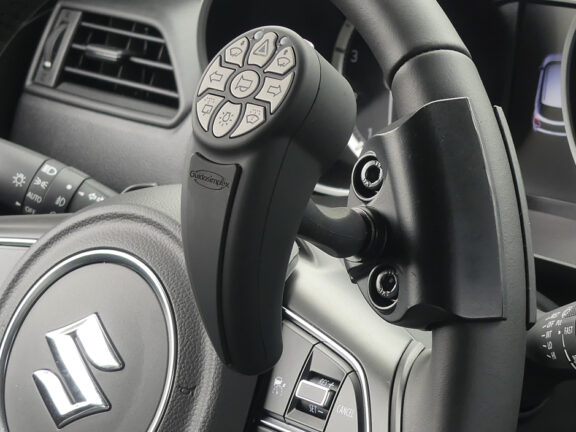 Closeup of StickSteer controller attached to a steering wheel on a pivot to allow one handed use of the controller whilst steering the car.