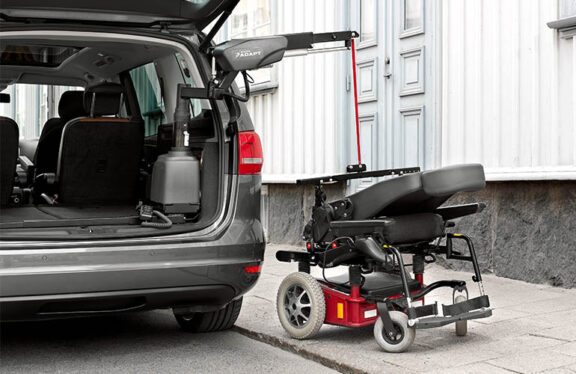 A mobility scooter is attached to the carolift vsl 6900 hoist that extends from the open boot of an adjacent van.
