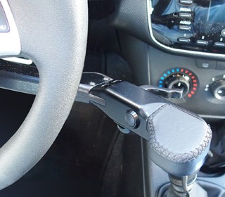 Close up of the front trigger throttle with push brake fitted on the right hand side of a steering wheel. There is a small trigger on the side nearest the dashboard, and a lever arm extending off the left behind the steering wheel.