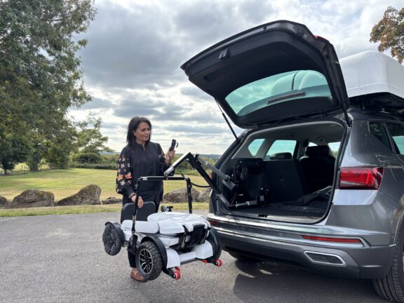 A folding Robooter X40 is lifted into an open car boot by an Apex Assist Hoist
