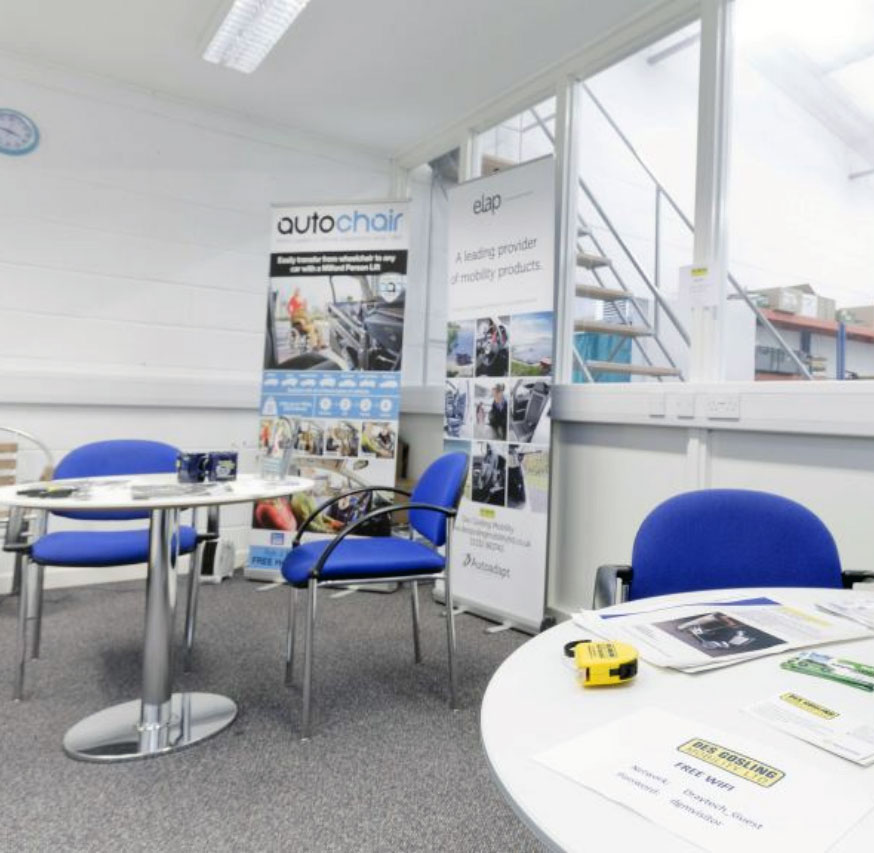 Customer Waiting Area inside Workshop. Blue chairs sit at tables covered in informational and promotional material, a window behind shows the workshop.