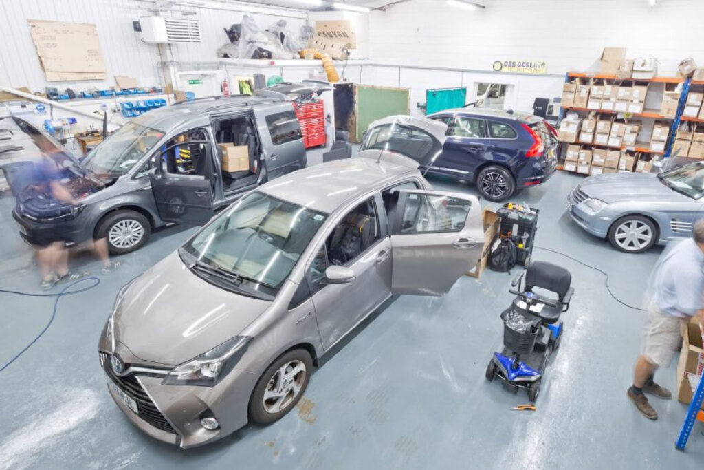 Photo from top corner of the workshop showing 4 cars being fitted with mobility adaptations with blurry engineers from long exposure time.